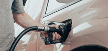 Closeup Of Man Hand Holds Black Gas Pump Nozzle Pouring Gasoline Into The Fuel Tank Of A Vehicle At Self Service Petrol Station. Grey Truck At Gas Station Refueling Petroleum By A Car Driver.
