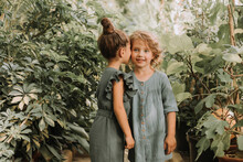 Two Beautiful Little Girls Of Different Nationalities Walk In The Botanical Garden Surrounded By Tropical Leaves And Keep Secrets. High Quality Photo