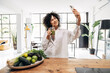 © Daniel - Young smiling african american woman takes selfie drinking green juice reusable bamboo straw in bright loft apartment