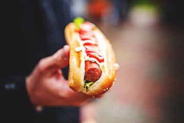 man holds fresh hot dog with ketchup in hands. Street food, fast food.