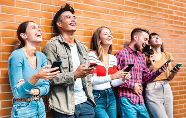 Multicultural friends laughing using smartphone at wall on university college campus - Young people addicted by mobile smart phones - Technology concept with always connected milenials - Vivid filter