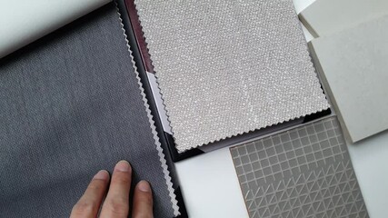 interior designer's hand selecting fabric on drapery catalog with others interior material samples such as white stone ceramic tiles, grey graphic tile samples and upholstery catalog.