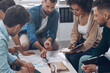 © gstockstudio - Top view of confident business team analyzing data while sitting in the office together