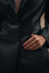 Wall Mural - Female hands with silver rings in the pockets of a black long leather jacket. Style, design of women's clothing. Vertical