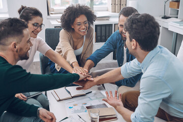 Poster - Confident young business team keeping hands clasped and smiling while sitting in the office together