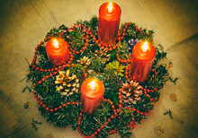 Close Up Of Four Red Candles Burning On Advent Wreath On Evening. Merry Christmas, Advent Crown Decoration, 4th Sunday, Christmas Background. Advent Wreath With Candlelights On Table In Wintertime
