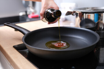 Woman pours olive oil into hot frying pan closeup