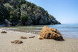 Leinwanddruck Bild - Sandstrand mit einer Muschel und Stein im Hintergrund Felsen uns Wasser