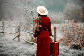 Woman in red coat, and hat with suitcase at snow countryside