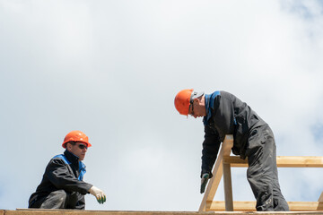 Repair of a wooden roof outdoors against a blue sky background. Two carpenters in special clothes work at a height. Roofing contractors are preparing the roof for the installation of insulation