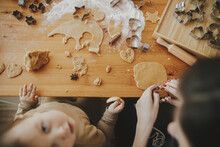 Cute Daughter And Mother Making Together Christmas Cookies On Messy Table, Top View. Adorable Toddler Girl With Mom Cutting Dough For Gingerbread Cookies. Atmospheric Holiday Time. Family Together