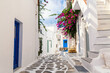 Famous old town narrow street with white houses and Bougainvillea flower. Mykonos island, Greece