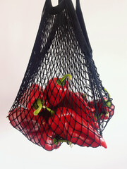 Sticker - Vertical shot of red peppers in a black string bag isolated on a white background