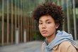© WHstudio Leushin N - Outdoor shot of serious young African American woman with confident face expression dressed in hoodie looks directly at camera poses against blurred background rests after strolling at city.