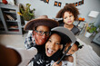 © Seventyfour - POV shot of excited African-American kids wearing Halloween costumes at home and taking selfie looking at camera