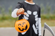 © Seventyfour - Close up of unrecognizable teenage boy holding Halloween pail to camera and wearing costume, trick or treat background