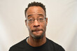© SarahJ - African American male wearing glasses looks into the camera while biting his lip.