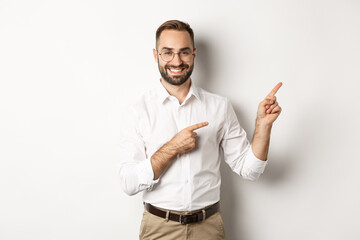 Wall Mural - Handsome successful businessman pointing fingers right, showing advertisement with pleased face, white background