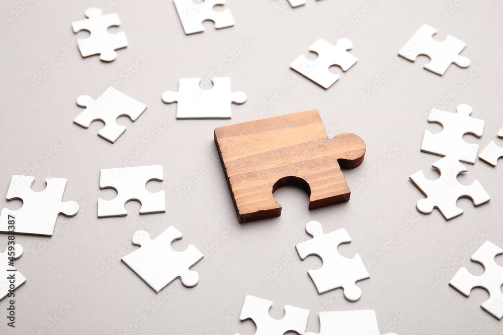 Wooden puzzle piece among white ones on light background. Concept of uniqueness