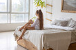 portrait of thoughtful beautiful teenage girl with long hair in white shirt and denim shorts on chair in bedroom decorated with dried flowers, mirror and minimalistic cozy Scandinavian design