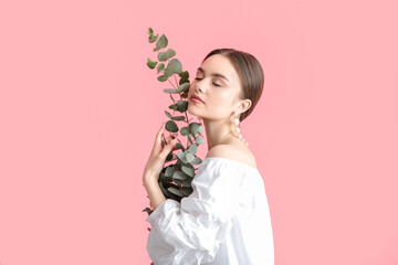 Beautiful young woman with eucalyptus branches on color background