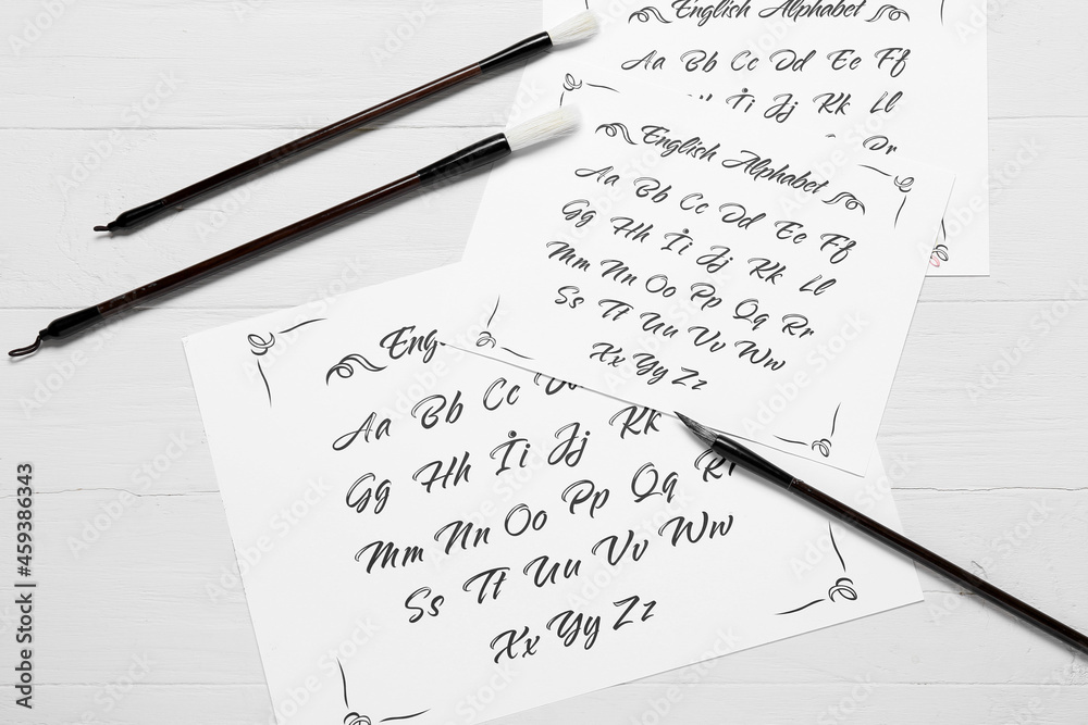Paper sheets with alphabet and brushes on white wooden background