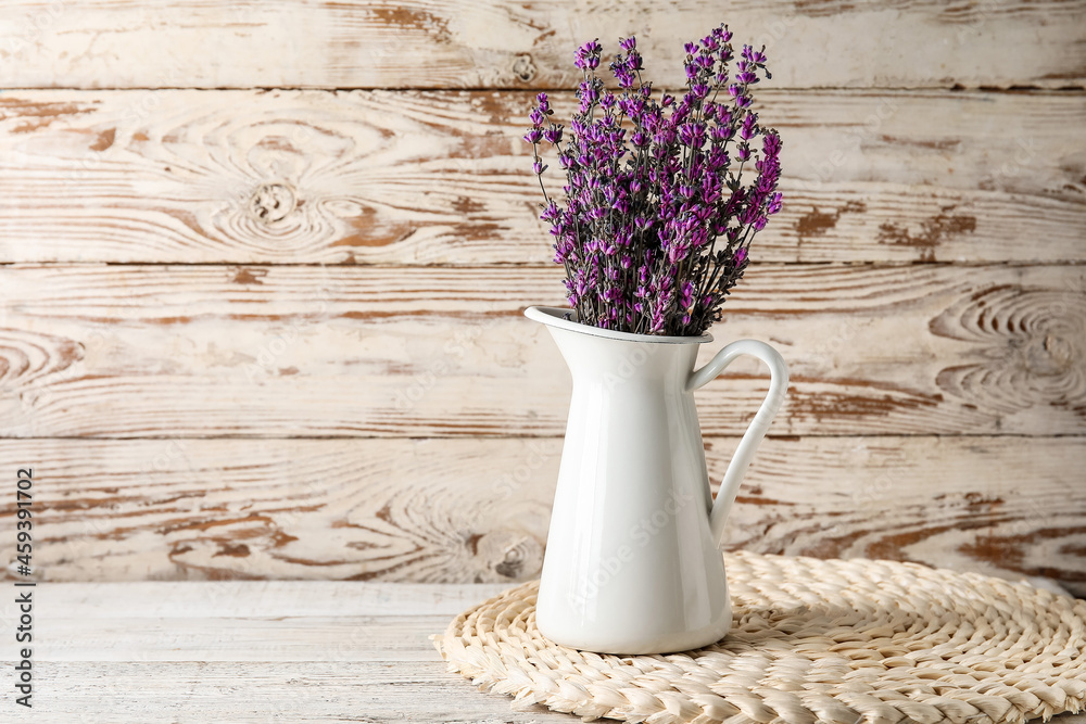 Jug with beautiful lavender flowers on light wooden background