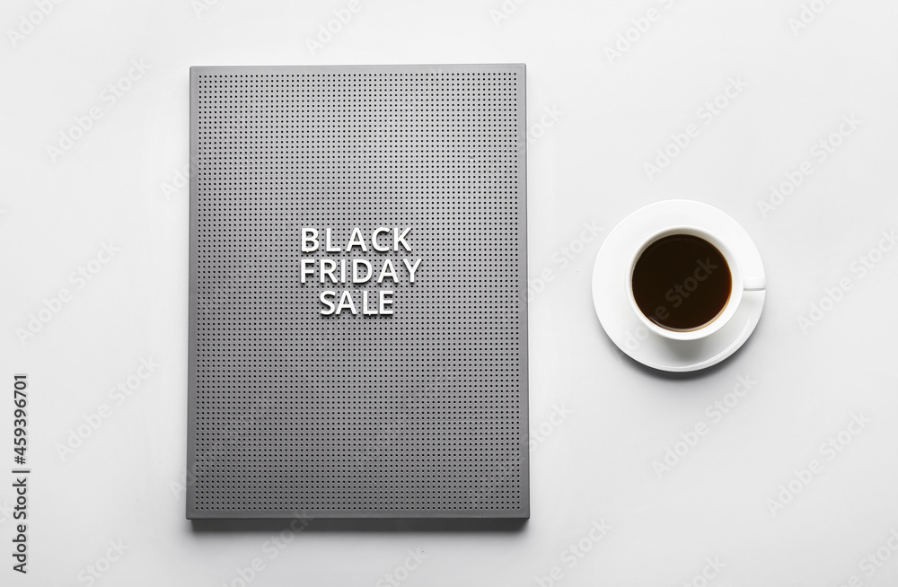Board with text BLACK FRIDAY and coffee on light background