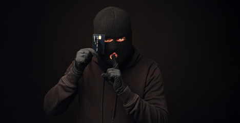 thief in black balaclava holding black credit card. banking and non cash thief concept