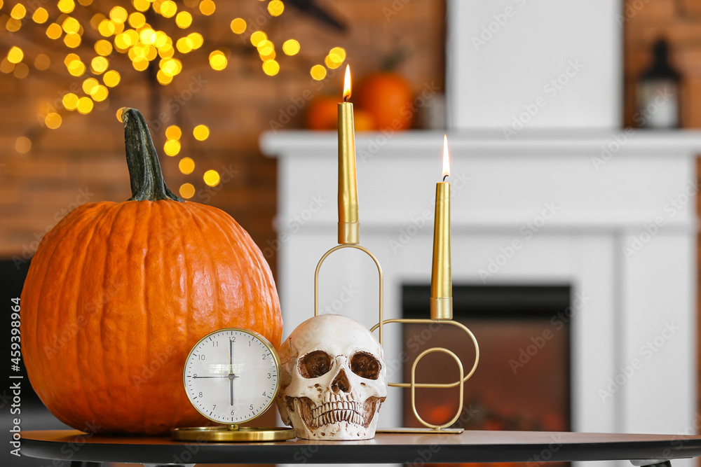 Human skull with alarm clock, candles and pumpkin on table in room