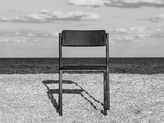 Black beach chair on empty sand beach with blue sea water background. Minimalism style autumn travel relaxation, spring fall vacation. No people, nobody, introversion psychology melancholia depression