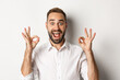 Close-up of amazed caucasian guy agreeing, showing okay signs and looking impressed, recommending product, white background