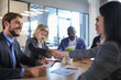 © ty - Two women shaking hands and looking at each other with smile while their coworkers sitting at the business meeting.