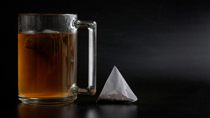 Wall Mural - Transparent mug and triangular pyramid tea bag on a dark gradient background. Free space for an inscription