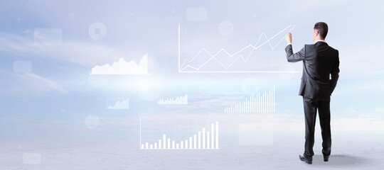 Poster - Back view of attractive young european businessman in suit standing on abstract blue sky with clouds background with business chart and graph. Finance and success concept.