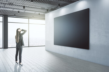Aufkleber - Attractive thoughtful young european businesswoman looking at empty black mockup banner in interior with city view and daylight. Gallery concept.