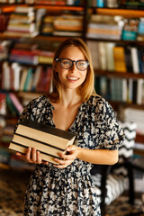 Back to school library concept. Student girl holding book on her hands on background of bookshelves in the library. Education and school concept.