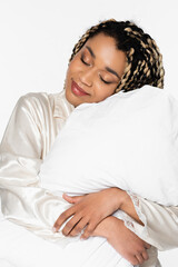 sleepy african american woman smiling with closed eyes while hugging pillow isolated on white