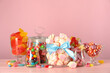 Jars with different delicious candies on pink wooden table