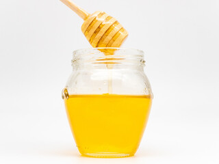 Wall Mural - Honey in a transparent glass jar with a wooden dipper isolated on a white background