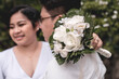A happy asian lady with her husband, after a simple garden wedding reception. Holding a white floral bouquet.
