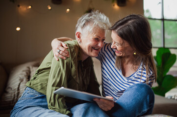 portrait of happy senior mother with adult daughter indoors at home, using tablet.