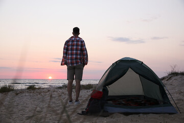 Wall Mural - Man enjoying sunset near camping tent on beach, back view