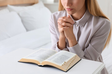 Wall Mural - Religious young woman with Bible praying in bedroom, closeup