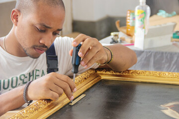 Wall Mural - Hispanic male restoring a vintage golden frame