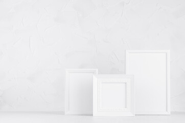 Collection of different white wood blank rectangle and square photo frames in soft light interior on wood floor and plaster wall, copy space. Template for presentation, portfolio, design, advertising.