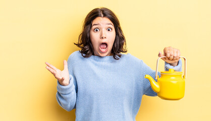 Wall Mural - young hispanic woman feeling extremely shocked and surprised. teapot concept