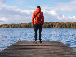 a young man in a bright orange hoodie on a wooden pier against the background of the lake. autumn ti