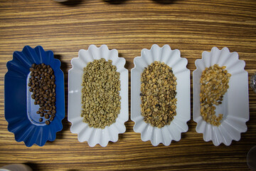 Poster - Top view of four plastic plates with roasted and raw coffee beans on a wooden table