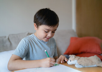 Wall Mural - Schoolboy using green colour pen drawing on white paper sheet, Young kid doing school homework, Happy mixed race child enjoy doing arts and crafts at home on weekend. Home Education